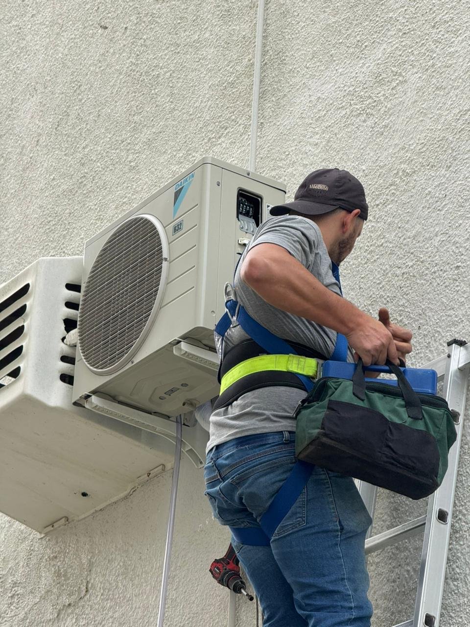 Técnico com cinto de segurança instalando condensadora Daikin em altura